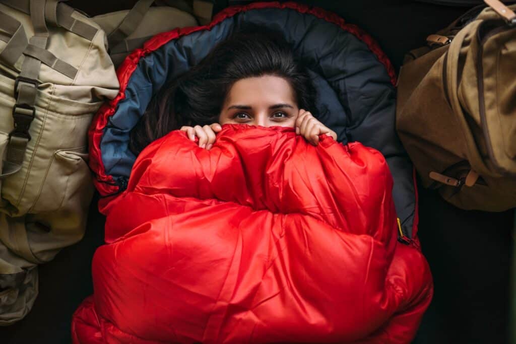 A woman bundling herself in a sleeping bag to keep warm in her RV.
