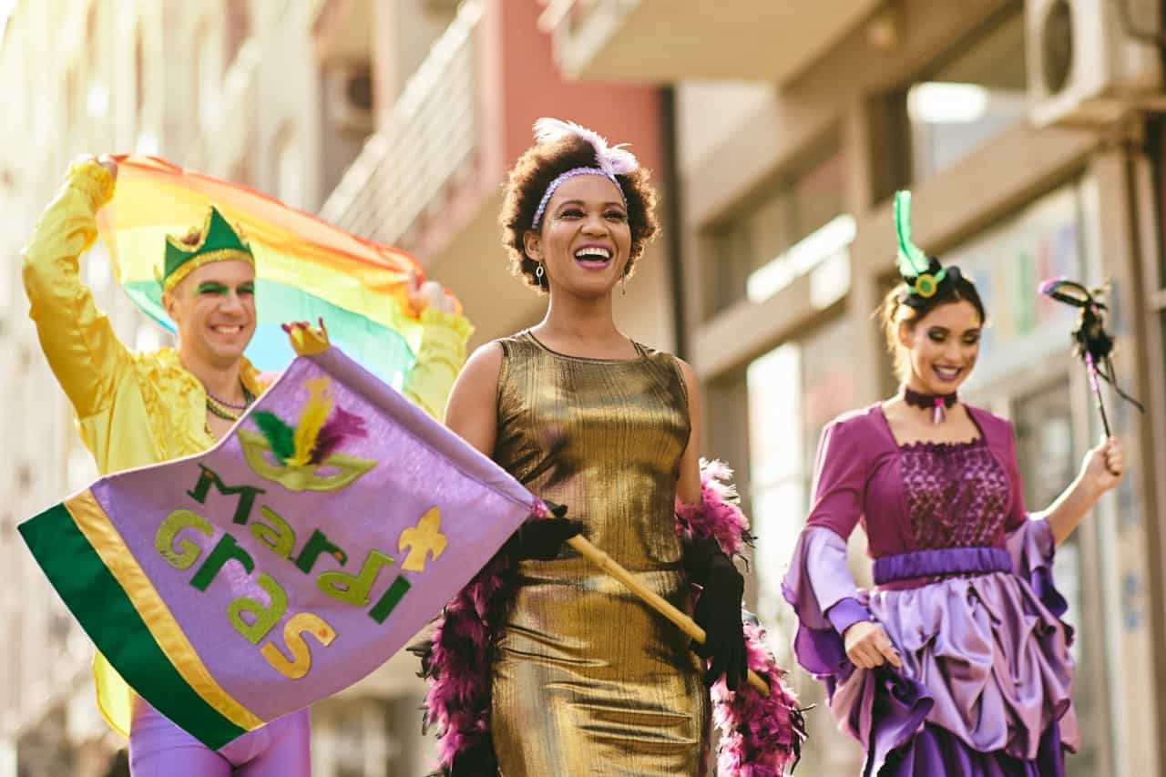 Three people in brightly colored outfits celebrating during Mardi Gras.
