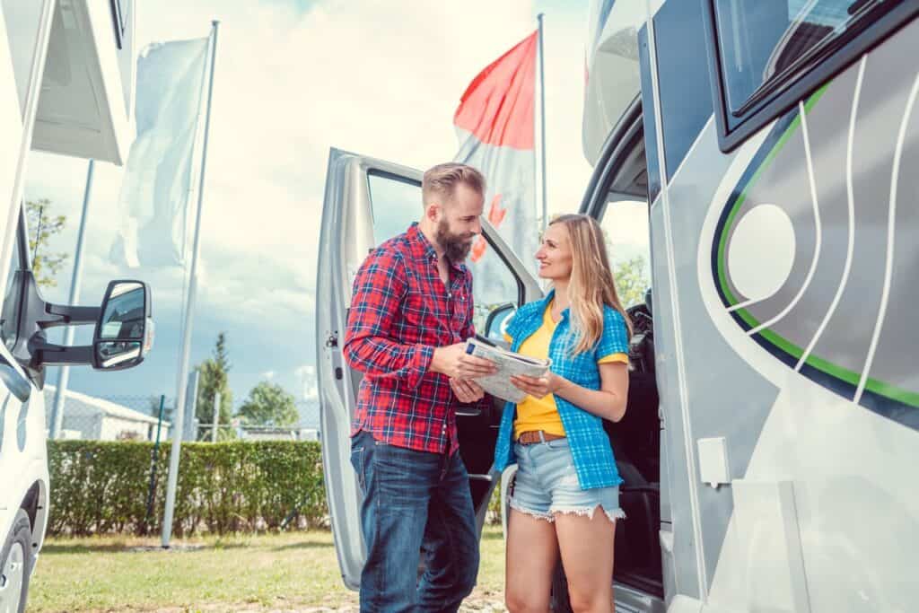 Man and woman looking at a map in front of an RV with the door open.