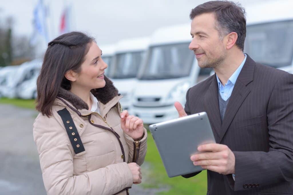 An RV salesman holding a tablet and talking to a customer.