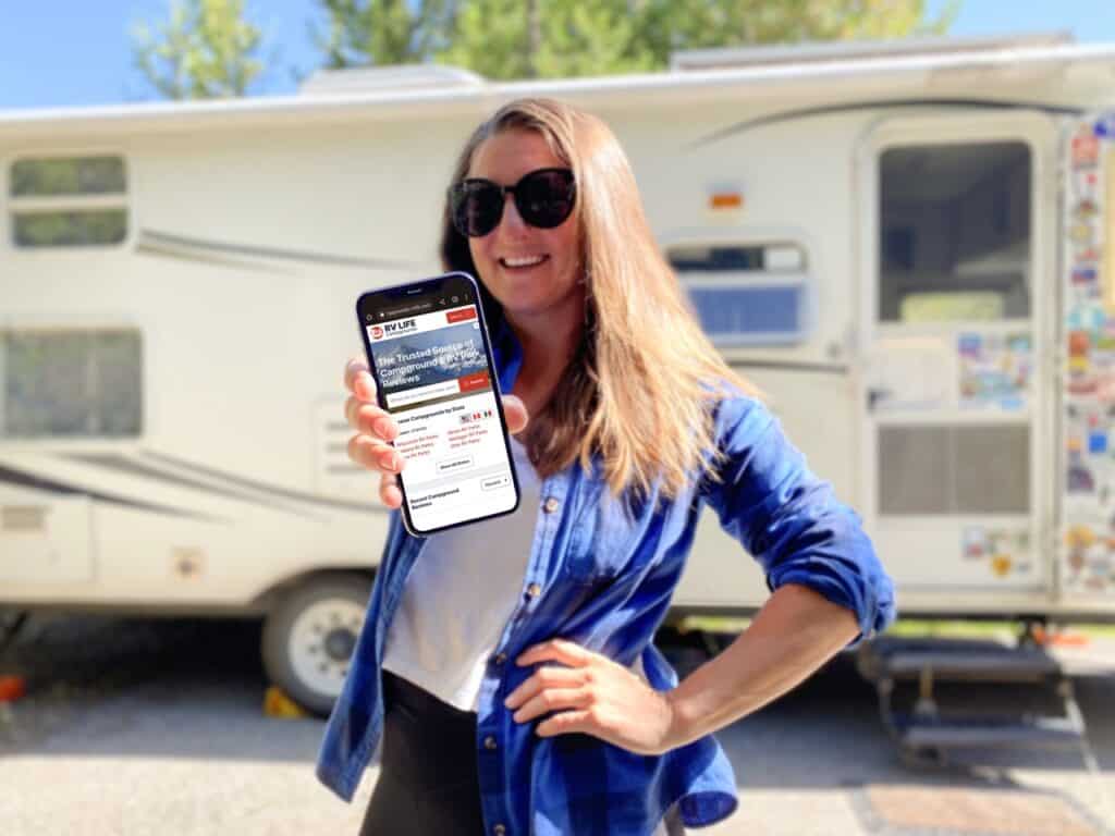 Girl in front of an RV with an iPhone that has RV LIFE app on screen.