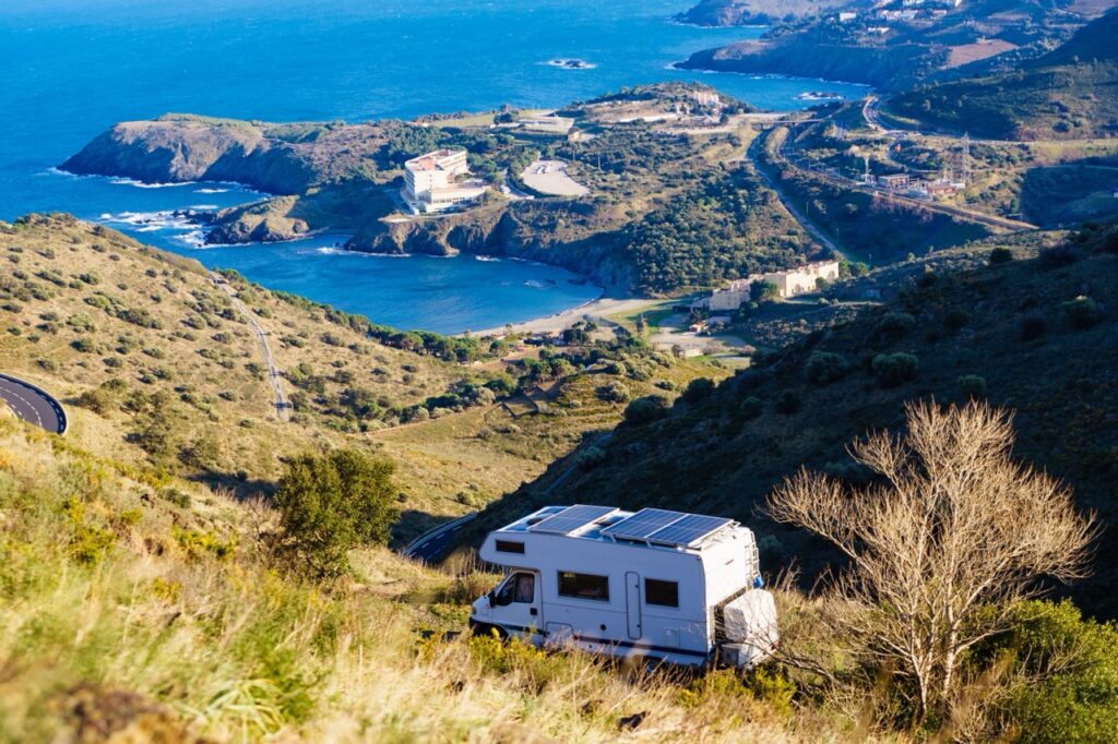 A Class C motorhome with solar panels in a remote location overlooking the ocean.